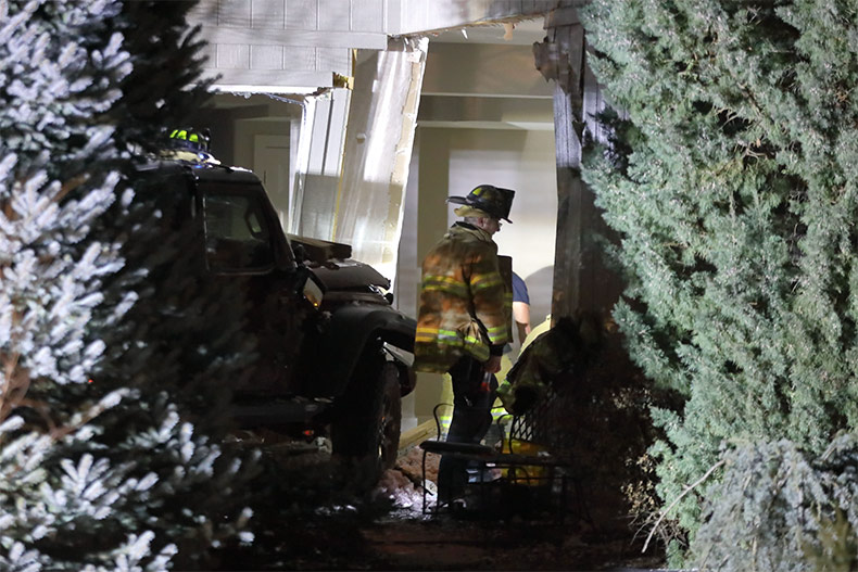 Firefighters working in the basement of the damaged house with the crashed Jeep just outside of the house.