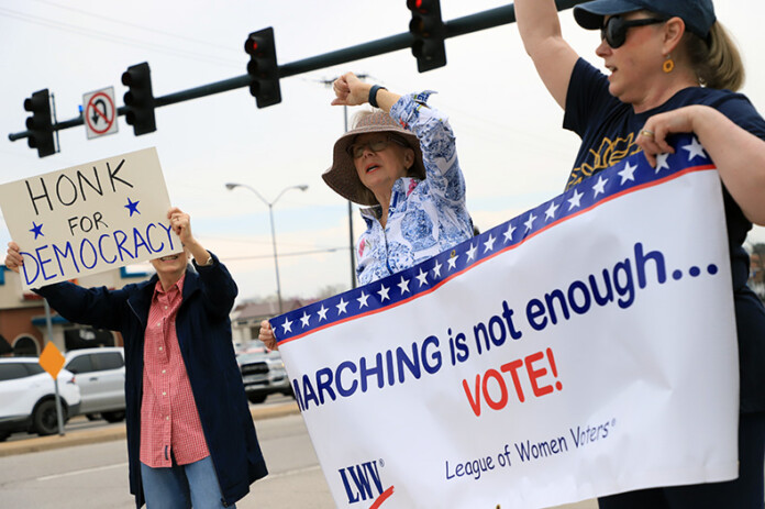 Members of the Johnson County League of Women Voters urge others to speak up about issues that matter to them during a protest at 95th and Quivira on Thursday.