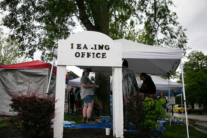 The sign for the leasing office is falling apart. Volunteers work quickly in the tent pavilions in the background.