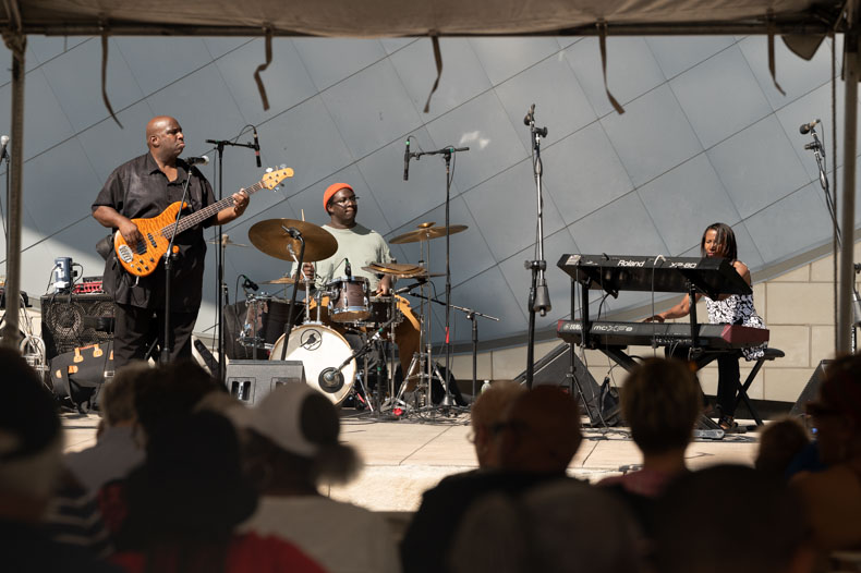 The James Ward Band, a family trio featuring James Ward (left) on bass, Jaylen Ward on drums, and Angela Ward on keyboards, opens the event with a performance. The band performs their jazz fusion repertoire regularly at The Blue Room and The Corvino Supper Club.