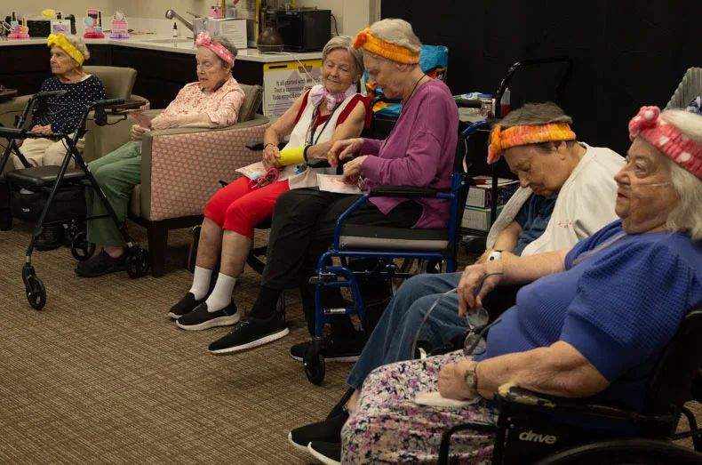 Assisted living residents attending Gorgeous Grandmas Day wait their turn for a facial and makeup, already sporting salon-style headbands and personalized gift bags. Residents received bracelets, affirmation cards, and more in their gift bags.