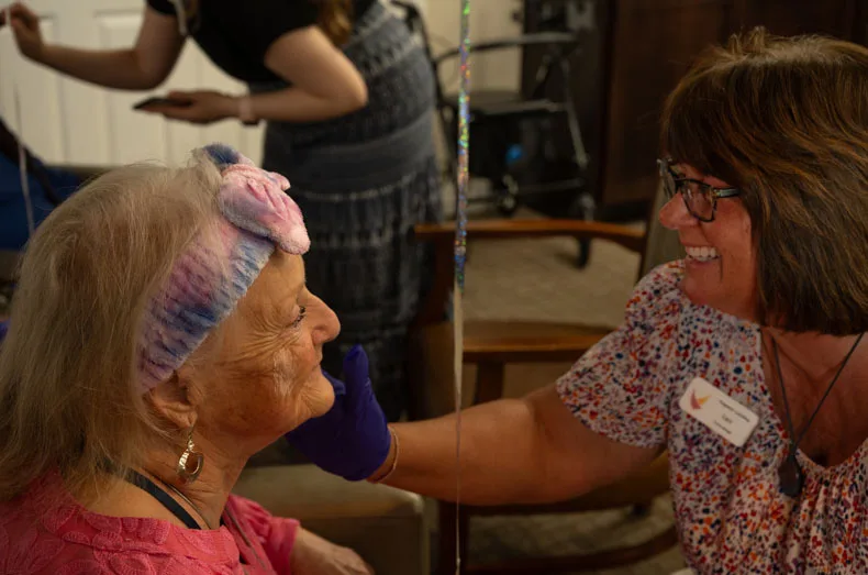 Lisa, a concierge at Pegasus Landing, laughs along with resident Kay as she applies lotion. “I’ve never had such a good [makeup] job,” said Kay.