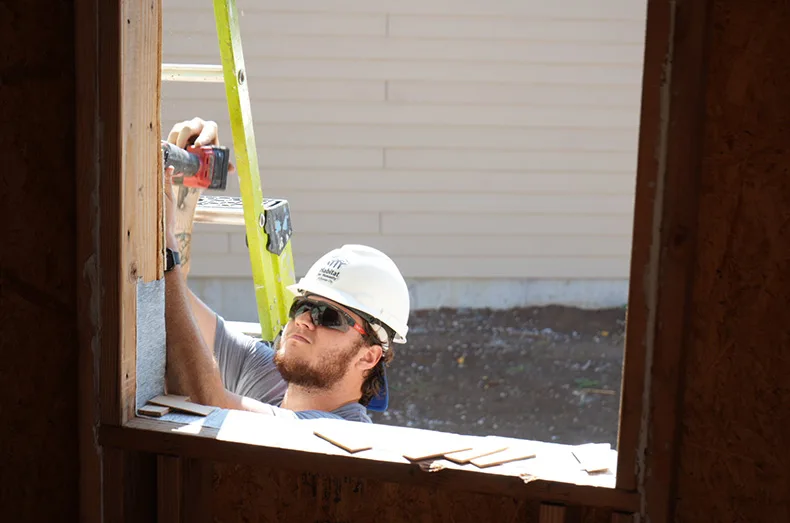 A volunteer from Foundation Recovery Systems makes adjustments to a window frame to better fit the window.