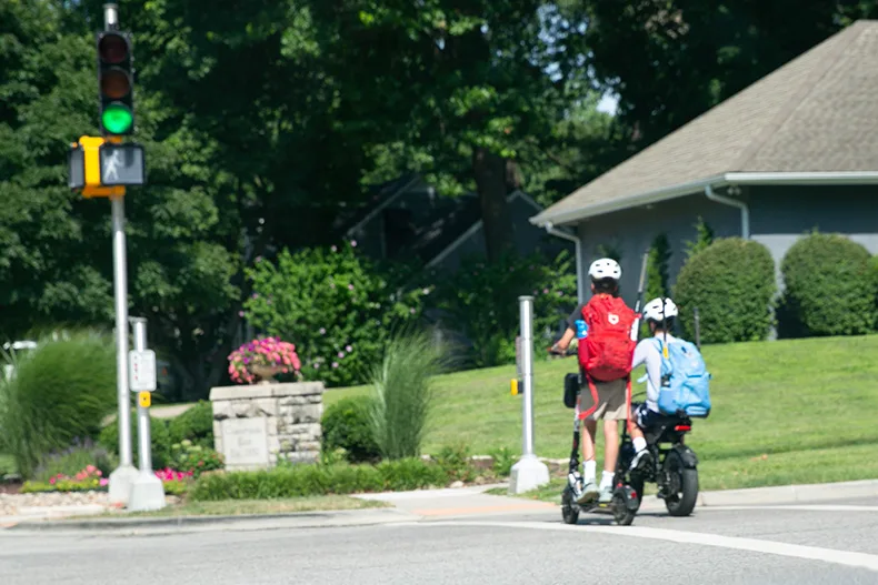 Two boys ride an e-scooter or an e-bike at 67th Street and Roe Ave.