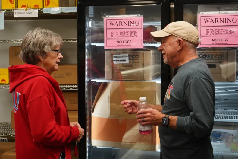 Two people talk in front of a commercial freezer.