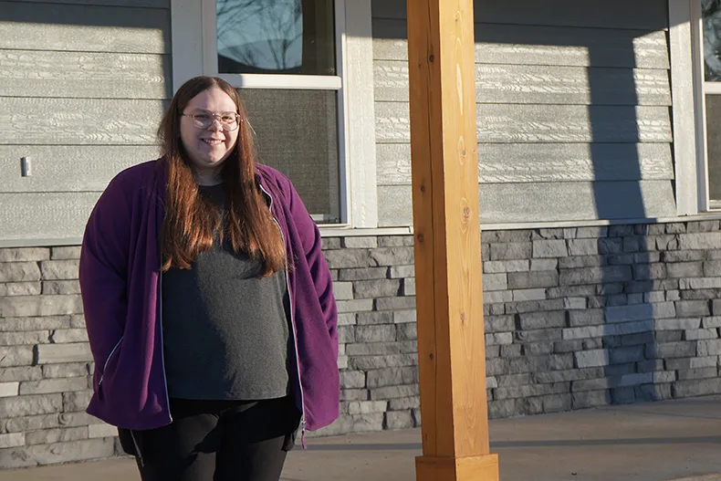 A woman stands in front of her house.