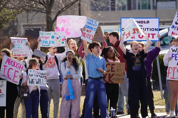 A group of teens stand on the sidewalk with signs.