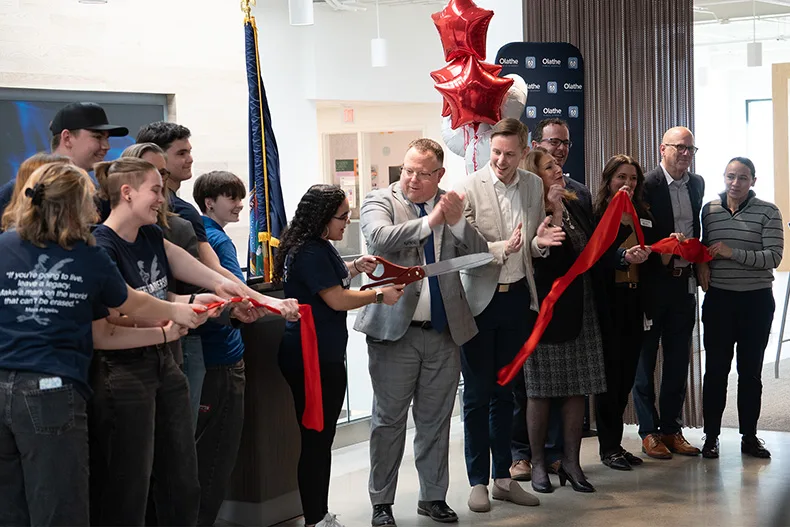 A group of people stand behind a ribbon after it's been cut. 