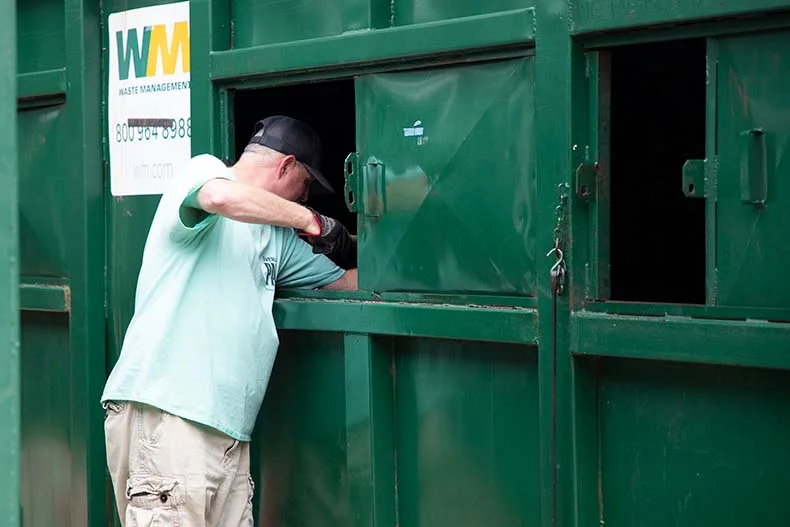Adam Hutchison, recycling center drop-off supervisor, fishes a non-recyclable item from a recycling bin.