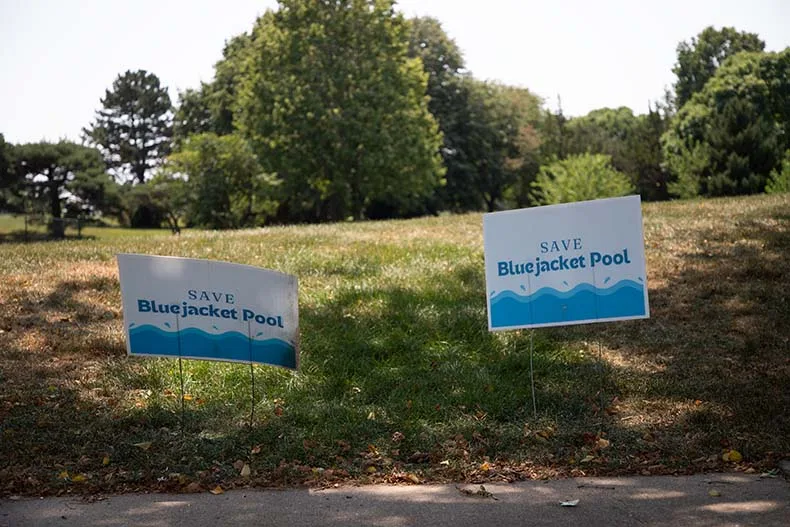 A Save Bluejacket Pool sign posted in front of the empty field where the pool used to be.