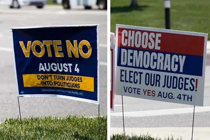 Yard signs urging voters to reject or support a constitutional amendment that would change Kansas' Supreme Court selection process.