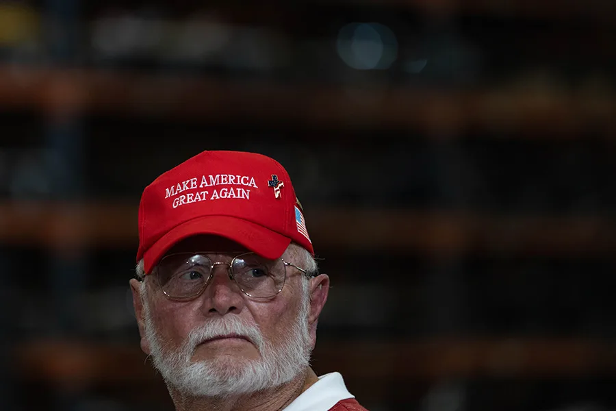 A man wears a “Make America Great Again” hat with an American flag cross.