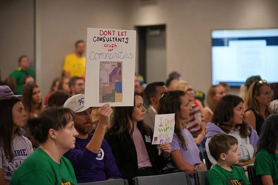 Ryan Van Pelt, Prairie Elementary parent, holds up a sign with a leaked draft of a boundary map that says, "Don't let consultants crush our communities," during Monday night's Shawnee Mission Board of Education meeting.