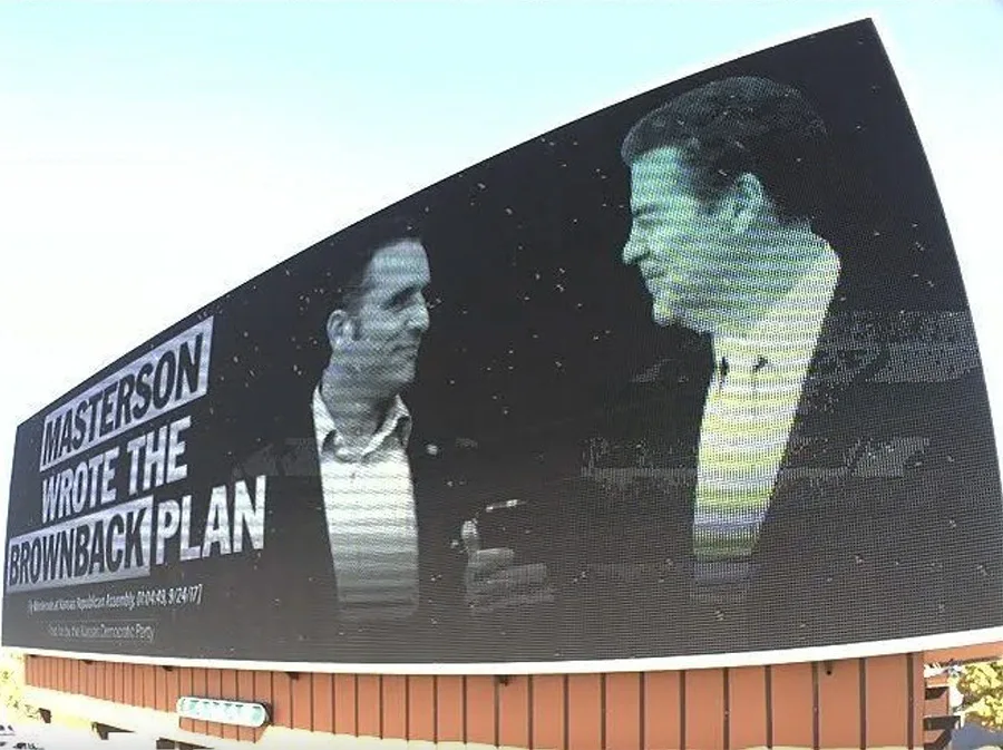 A Wichita billboard tying Masterson to former Kansas Gov. Sam Brownback, a common attack for Holscher, as both candidates attempt to appeal to moderate voters.
